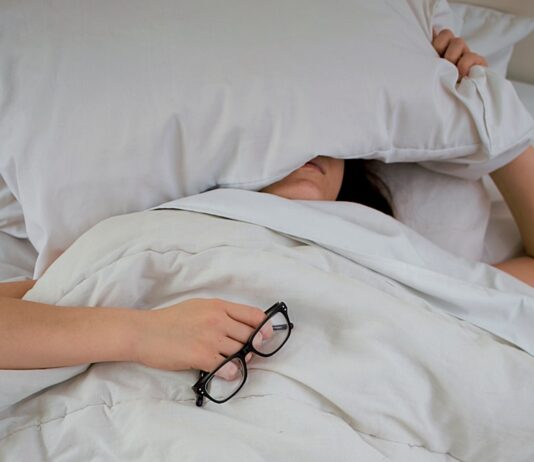 신체 회복과 면역력 증진 person lying on bed while covering face with pillow and holding eyeglasses