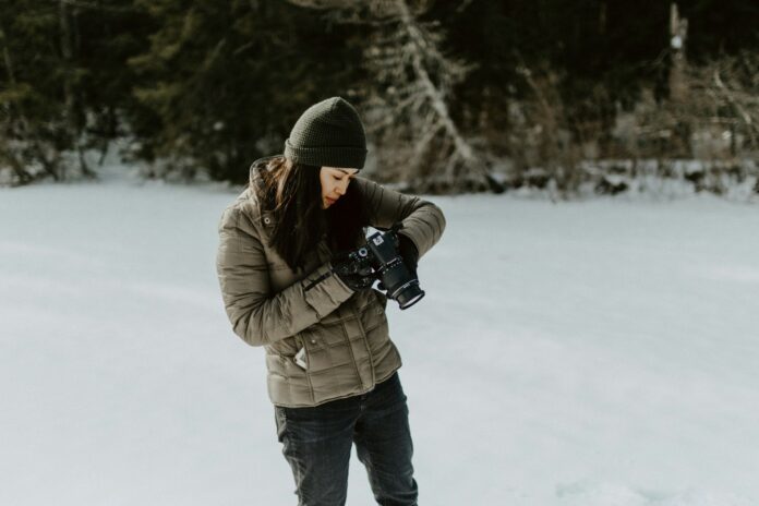 Photo by Kelly Sikkema woman holding black digital camera standing on ground filled with snow
