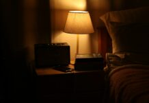 수면 혁명, 내 일상 속 꿀잠 길들이기…지금 실천할 수 있는 수면 건강 트렌드 A bedside lamp illuminates a nightstand with a radio.