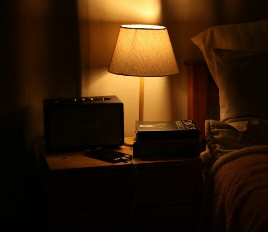 수면 혁명, 내 일상 속 꿀잠 길들이기…지금 실천할 수 있는 수면 건강 트렌드 A bedside lamp illuminates a nightstand with a radio.